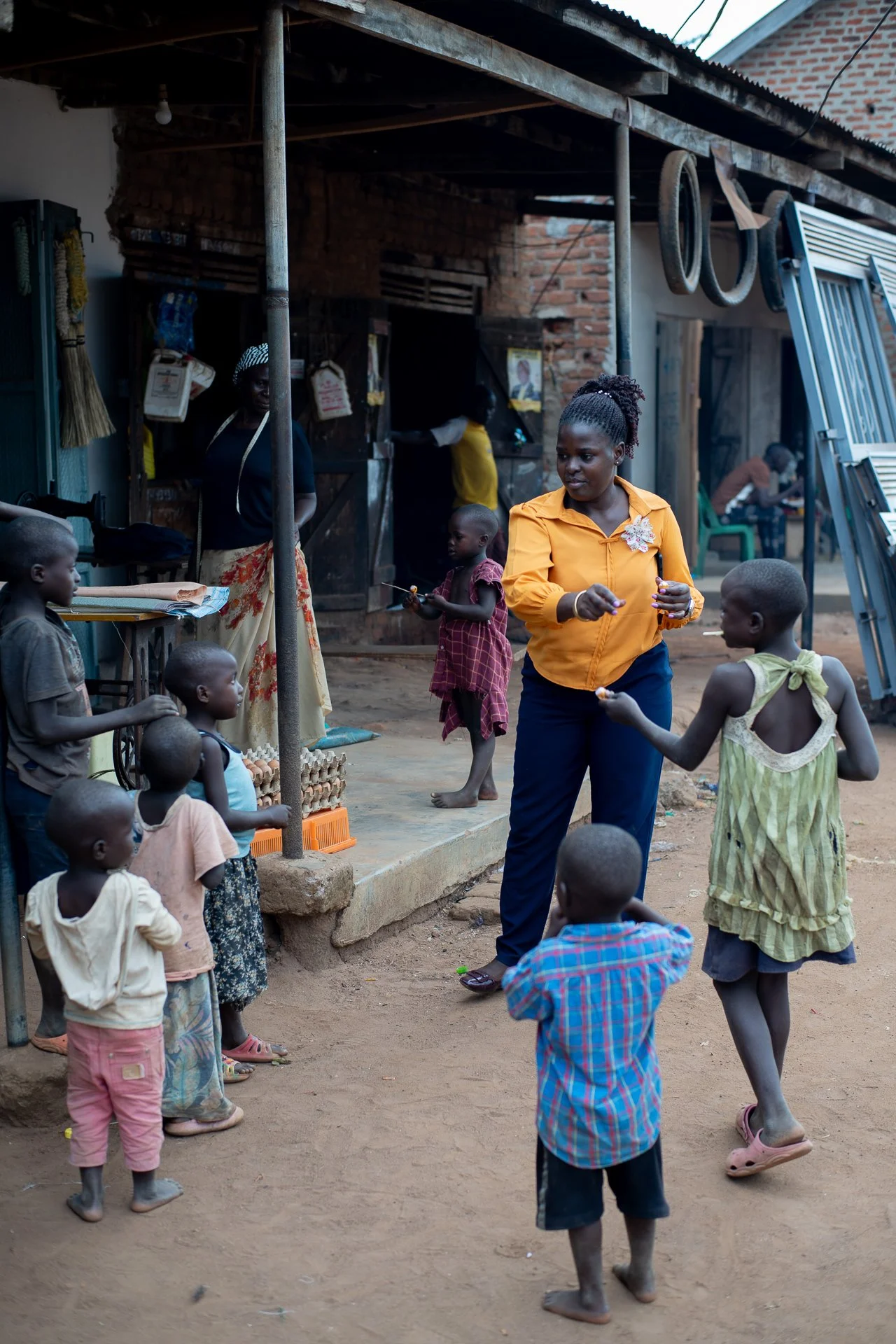 Eine Gruppe von Kindern und Erwachsenen auf einer Dorfstraße in Afrika, Kinder spielen und interagieren mit einer Frau, die in der Mitte steht und sich offenbar mit den Kindern unterhält.