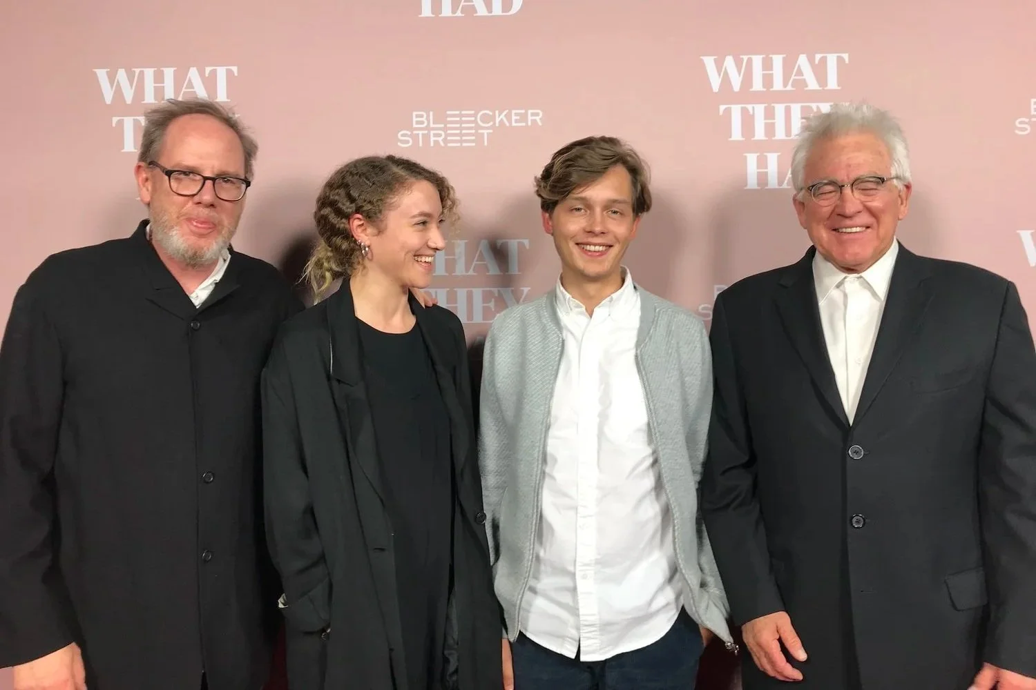 Vier Personen, zwei Männer und zwei Frauen, stehen vor einem Hintergrund mit Text. Sie lächeln und tragen formelle Kleidung.