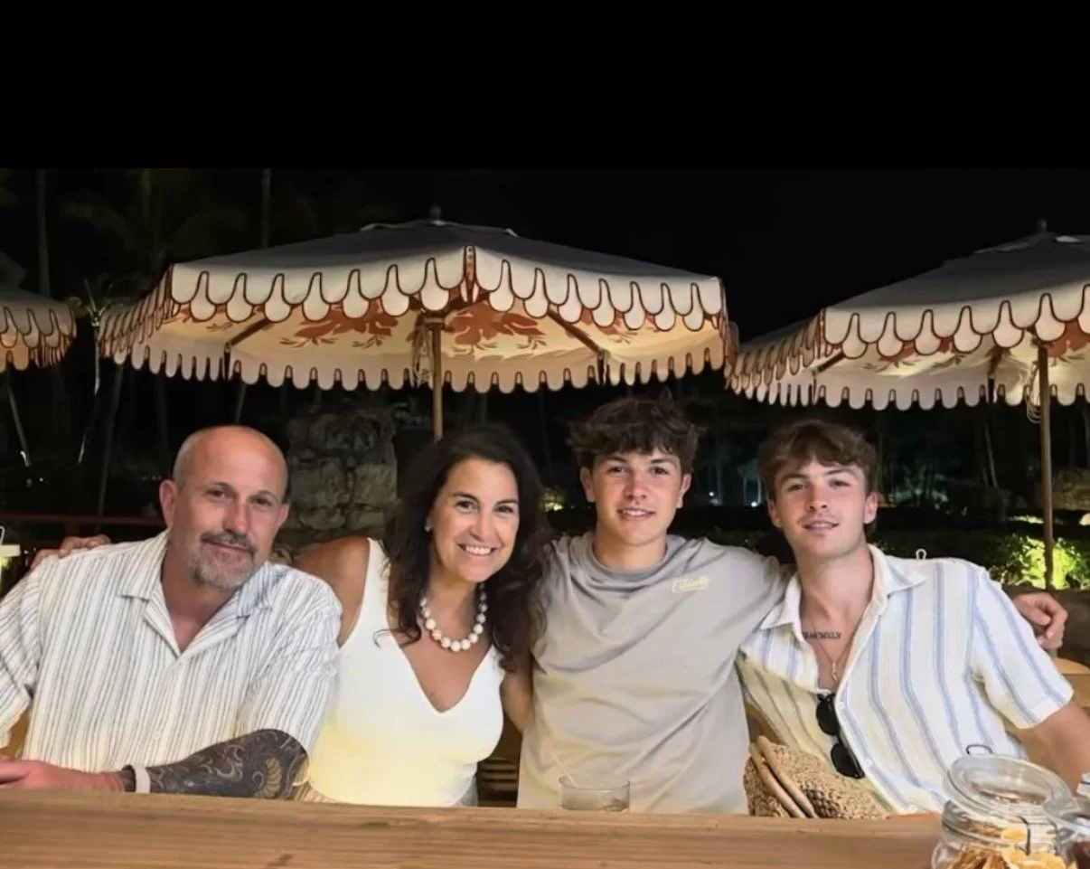 A family of four sitting at a wooden table outdoors at night, under large decorative umbrellas, smiling for the camera.