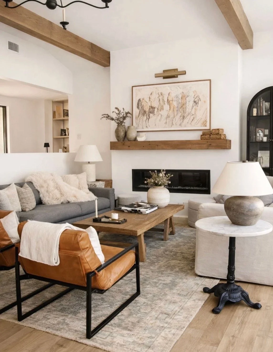 Bright, freshly cleaned living room with a gray sofa, tan leather chairs, a wood coffee table and exposed wood beams.