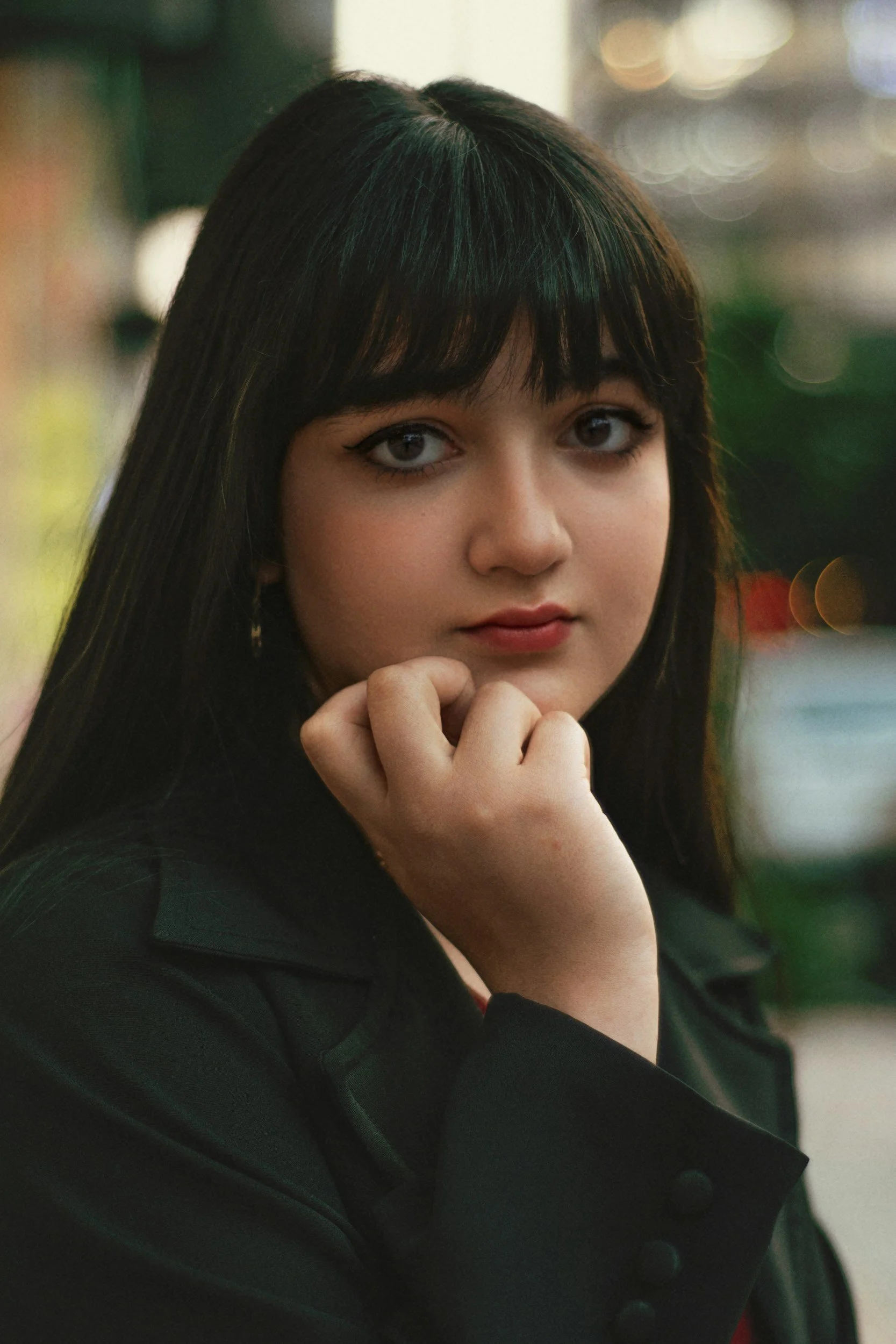 Woman's face with brown hair and bangs with her hand on her chin wearing red lipstick not smiling