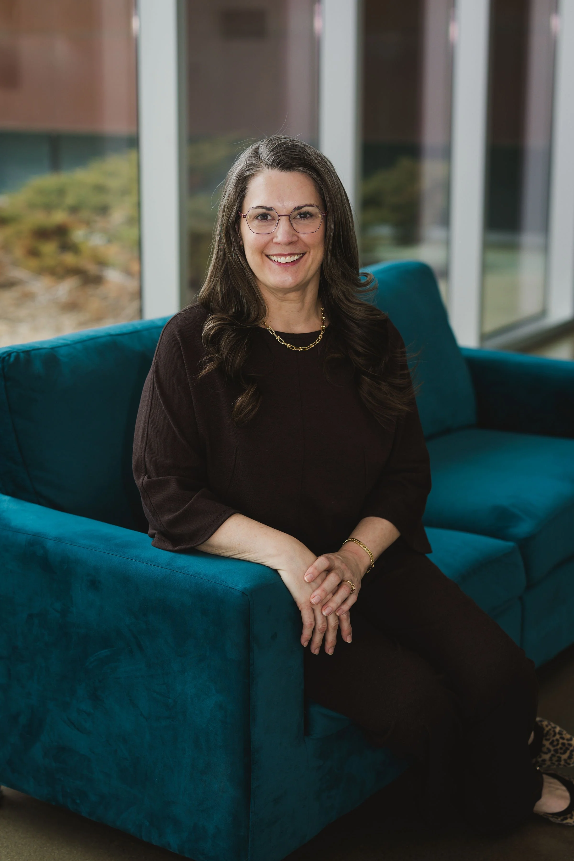 woman named heidi sitting on a blue sofa wearing a brown shirt smiling