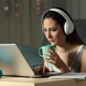 woman wearing headphones looking at computer holding a mug