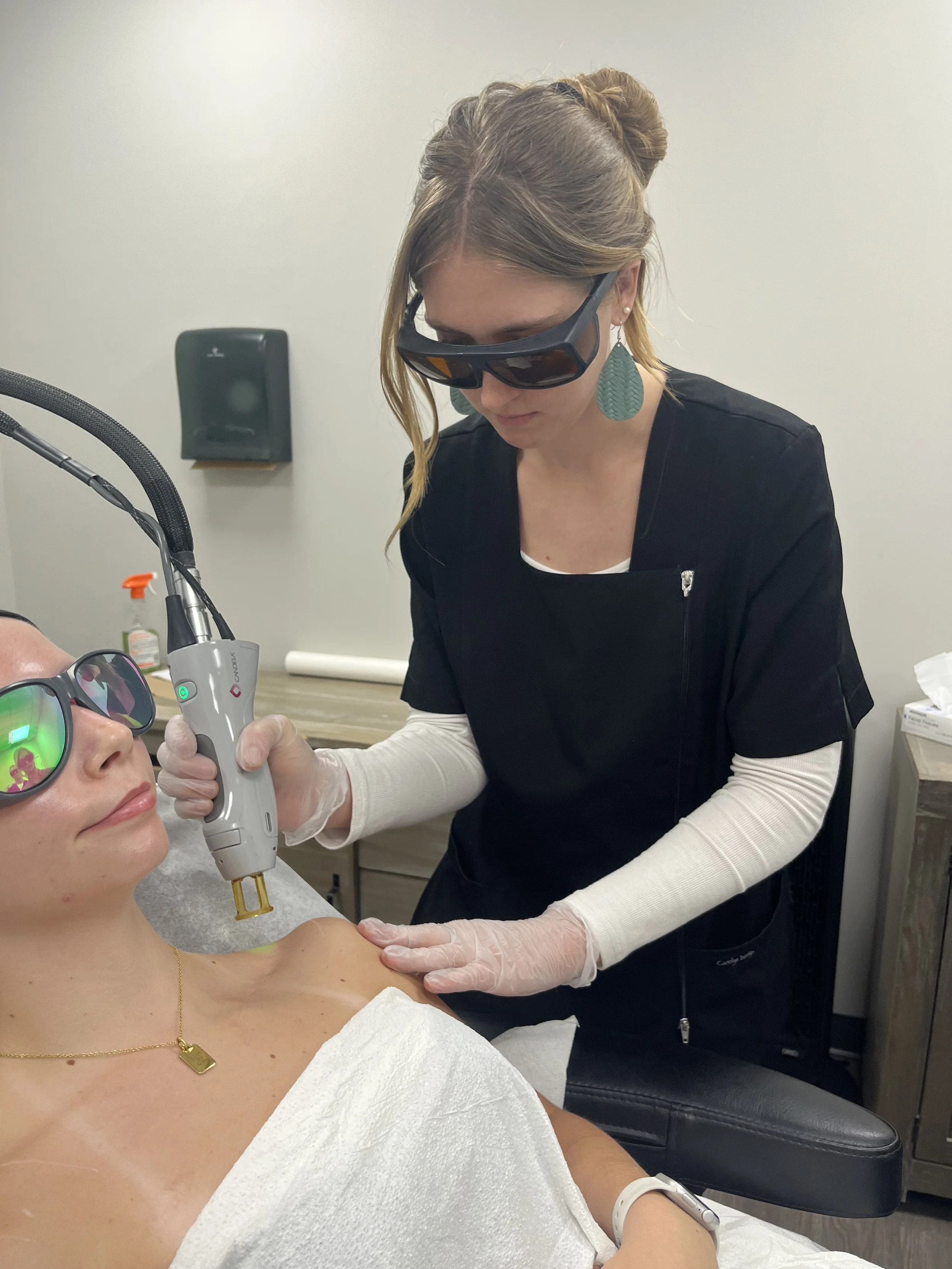 laser tech wearing black scrubs preforming laser hair removal treatment on a woman's shoulders