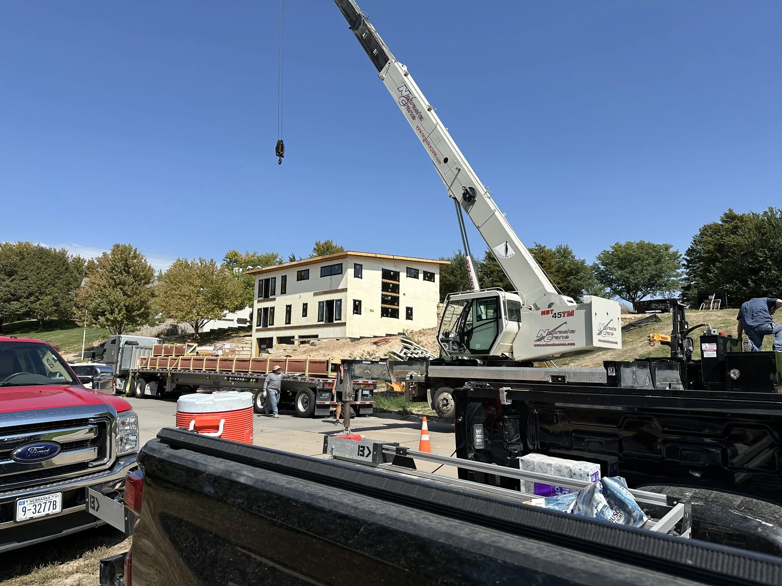 Construction site with a crane, unfinished building, trucks, and construction workers working outdoors under a clear blue sky.