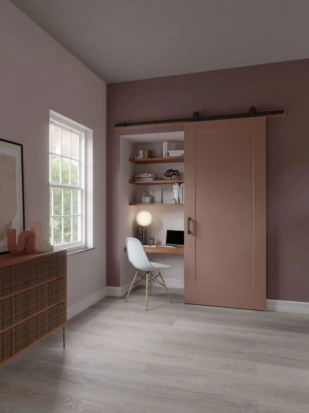 Home office area with a small desk, white Eames-style chair, built-in shelves with books and decor, a sliding barn door, a window with greenery outside, and a wooden cabinet with decorative items.