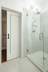 Modern glass shower enclosure in a white bathroom with a sliding door.