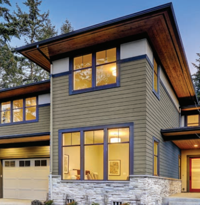 Modern two-story house with large windows, gray siding, stone accents, and a flat roof.