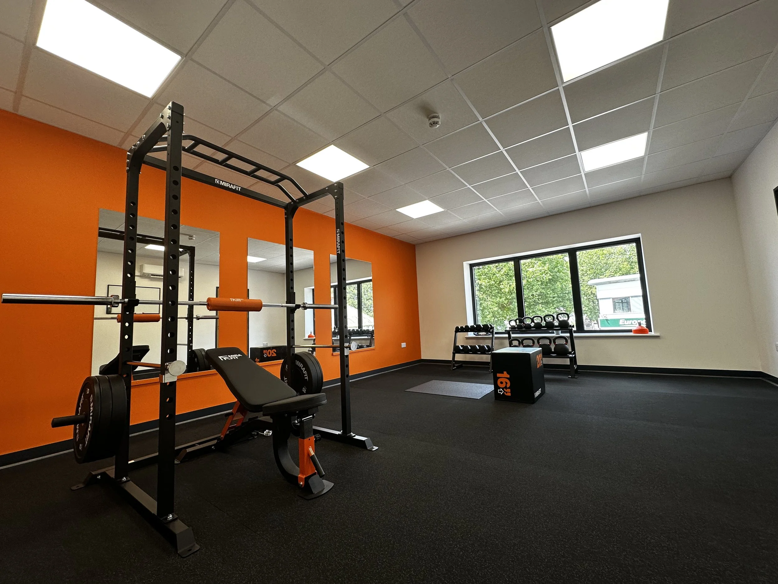 An exercise rehabilitation suite at Back On Track Chiropractic Clinic in Wolverhampton. Showing a bench press, squat rack, dumbbells, kettlebells. Allowing for exercise therapy for back pain, neck pain, hip pain, knee pain, sports injuries, and more.