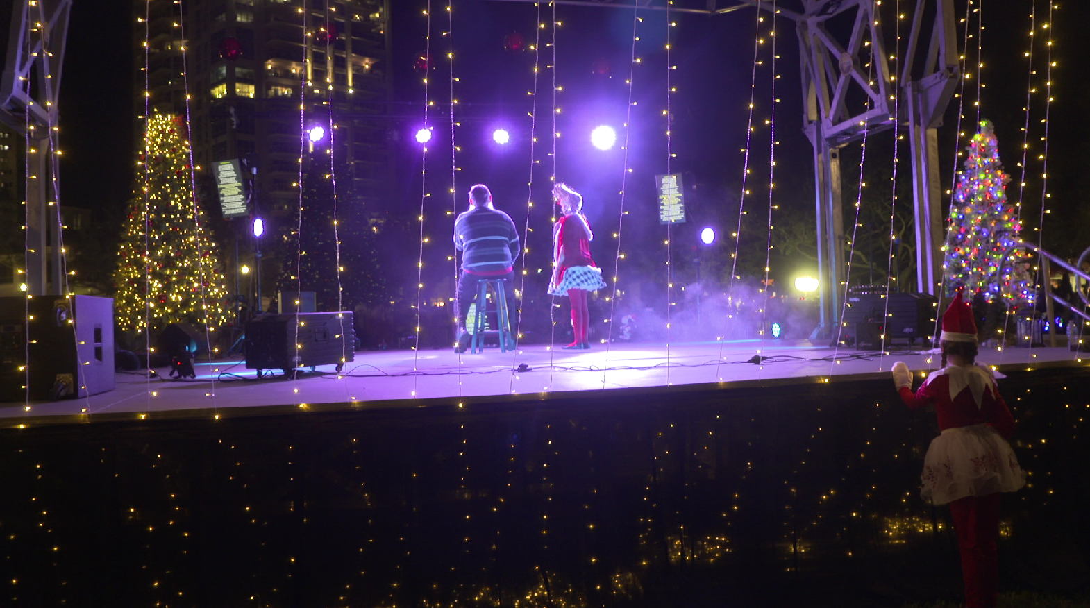 People performing on an outdoor holiday stage decorated with Christmas lights, including Christmas trees, at night. Tampa Bay Holiday Show Clearwater Florida