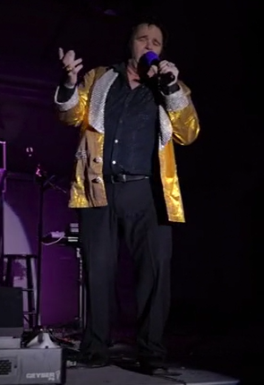 A man singing on stage with a microphone, dressed in a gold and silver jacket and black pants. Tampa Bay Holiday Show