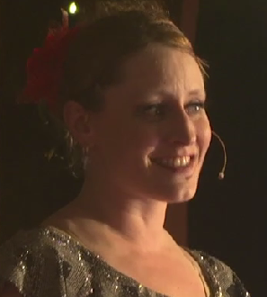 A woman with a big smile, wearing a sparkly dress and a red flower in her hair. Tampa Bay Holiday Show