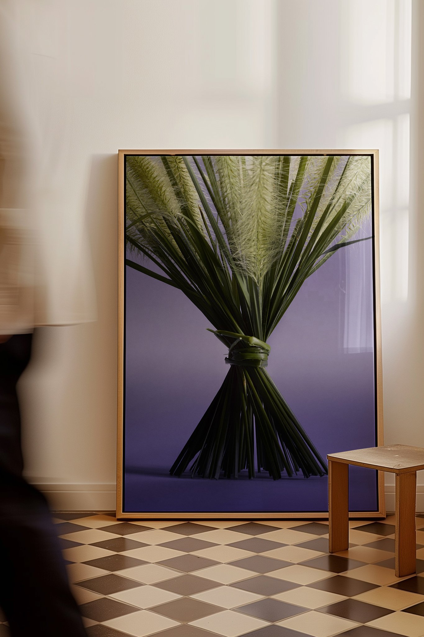 A framed large photo of a bundle of green plant stalks and leaves tied together, leaning against a wall in a room with black and white checkered flooring.