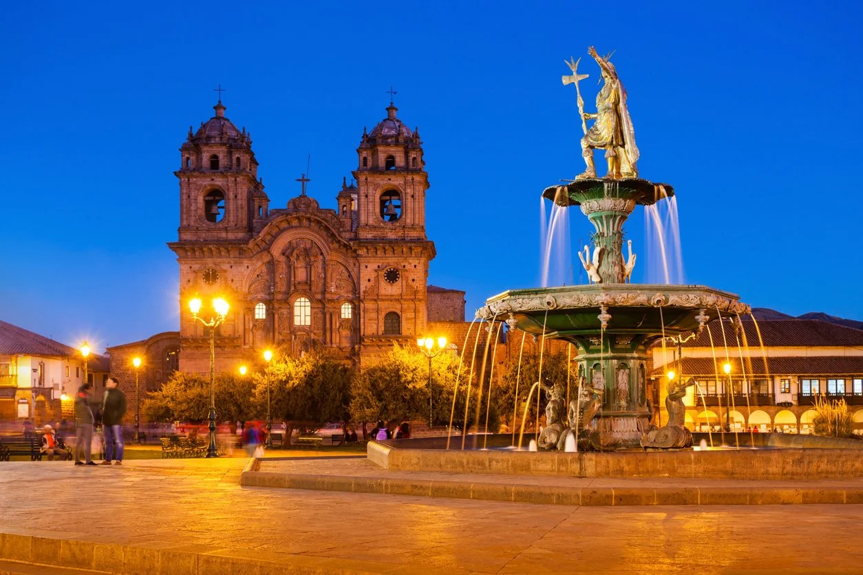 Historical cathedral and ornate fountain in a town square during evening with streetlights and people