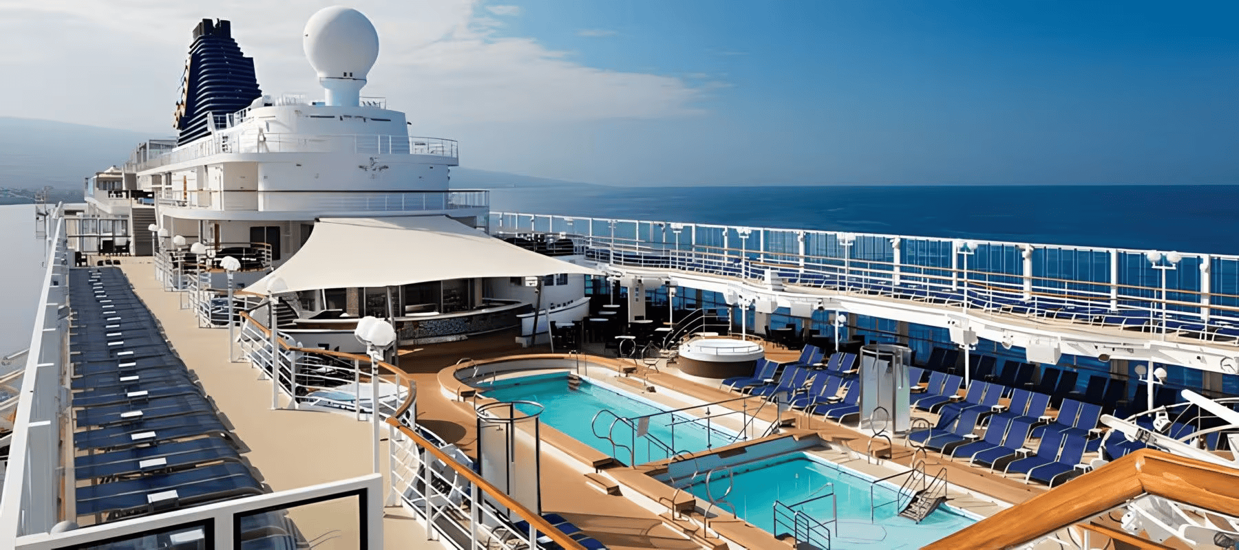 View of the outdoor swimming pools and sun loungers on the deck of a cruise ship with the ocean in the background during daytime.