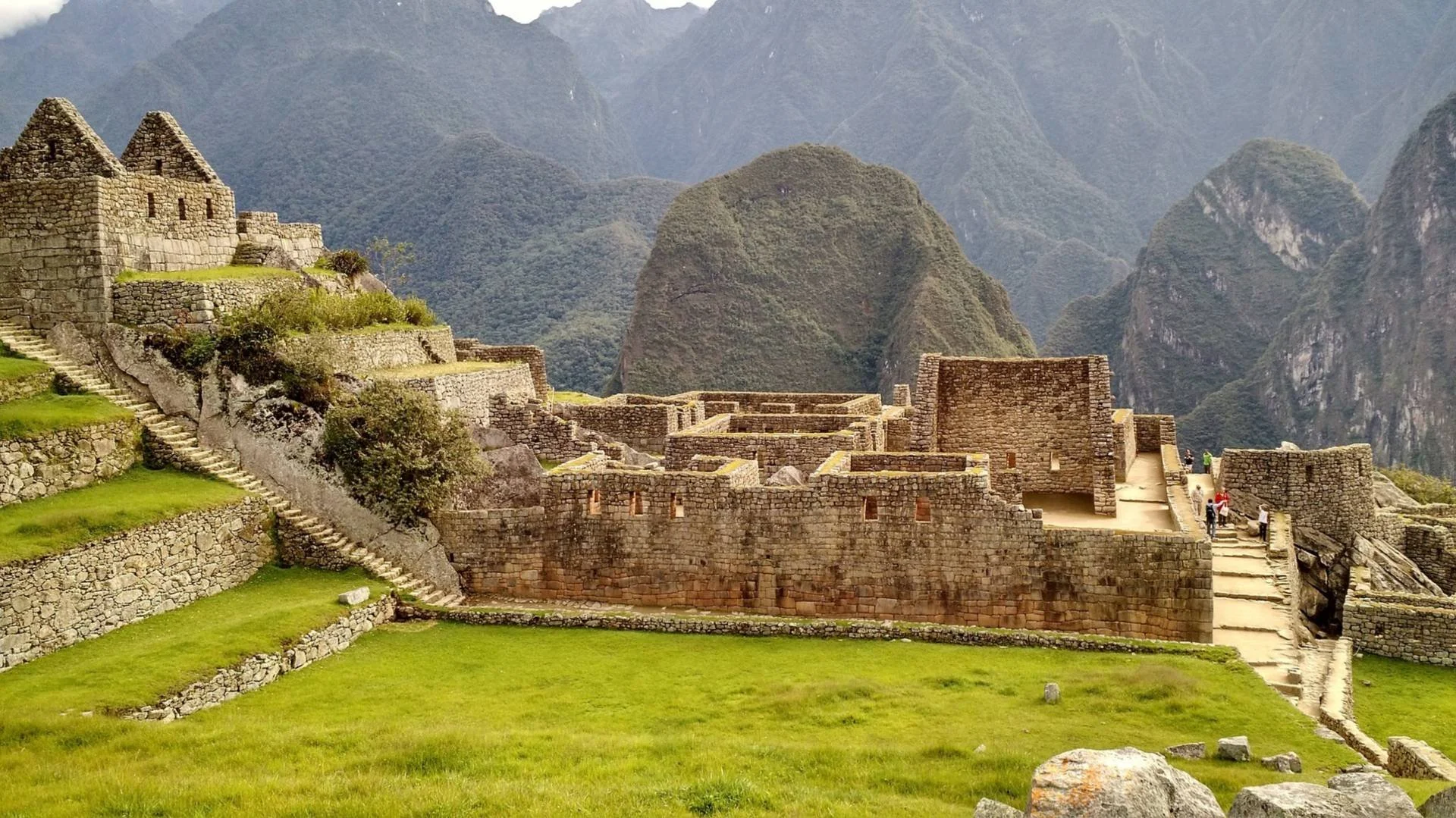 Ancient Incan ruins at Machu Picchu with stone structures, terraces, and lush green landscape surrounded by mountains.