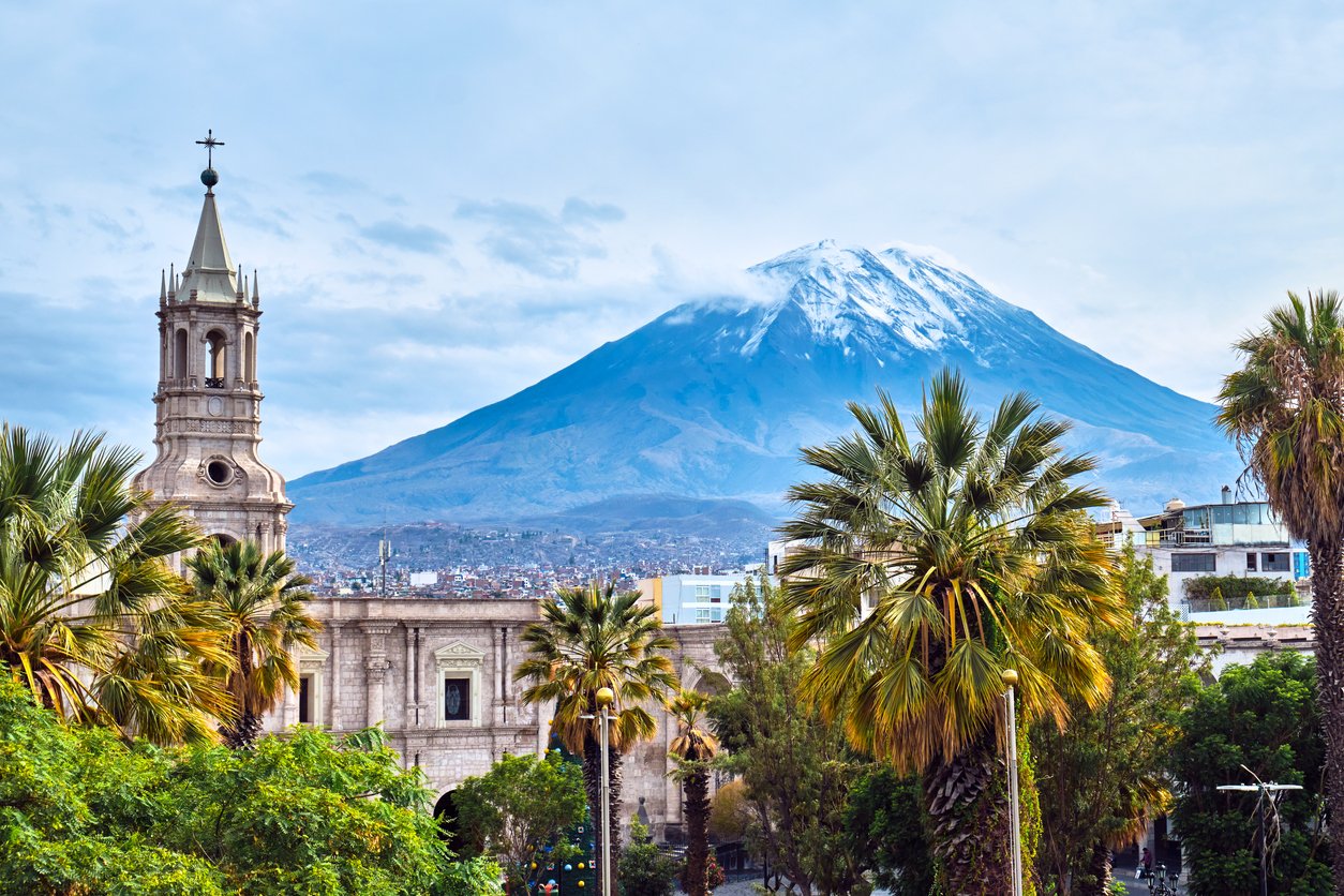 Cityscape with historic church and mountains, including snow-capped volcano, in the background