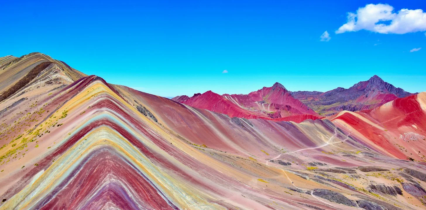 Colorful layered mountains against a bright blue sky with a few clouds.
