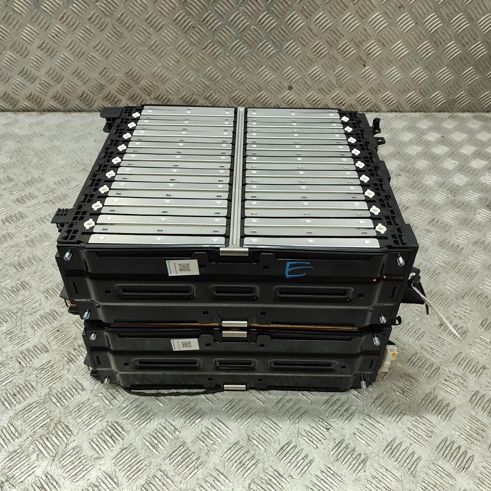 Stacked electric vehicle batteries placed on a metal floor with a diamond plate pattern.