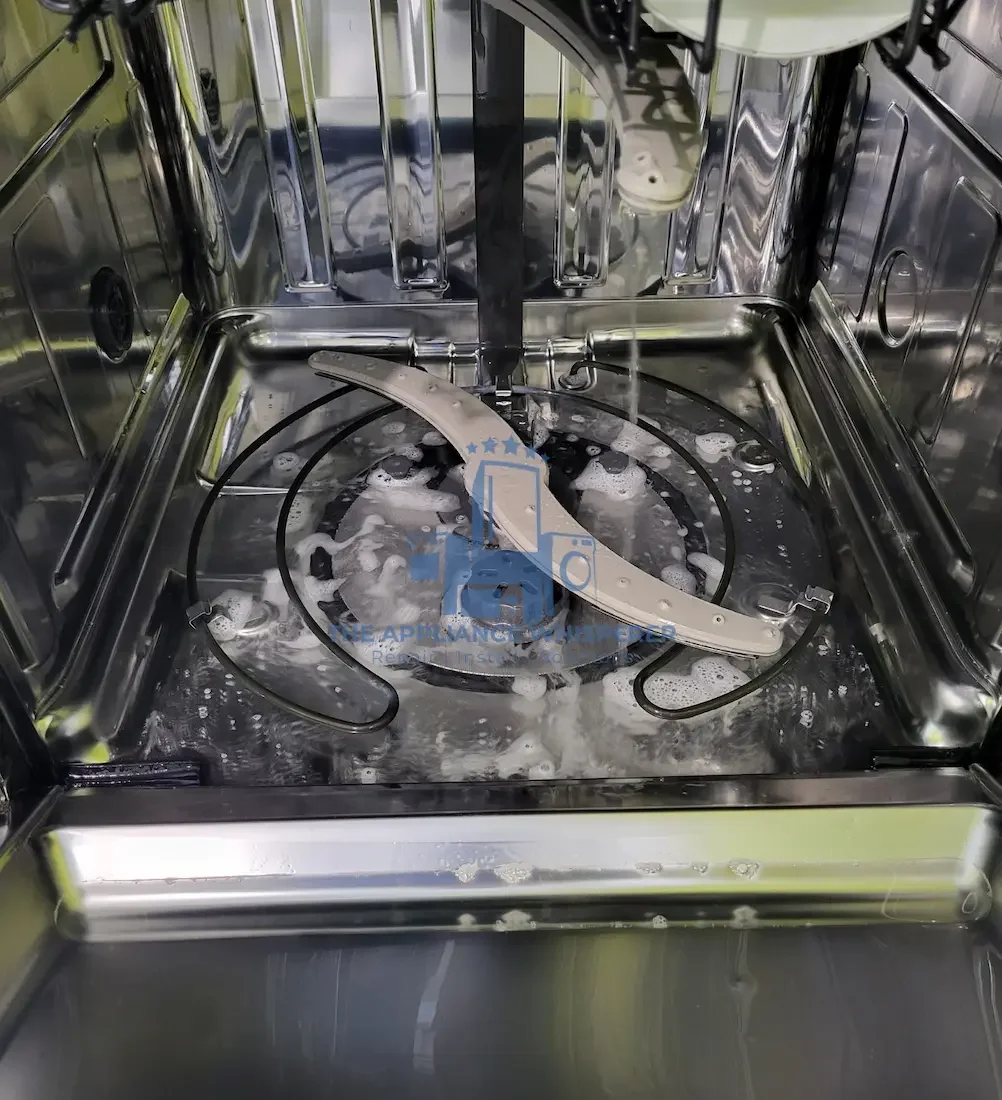 The inside of a stainless steel dishwasher with soap suds and a cleaning arm.