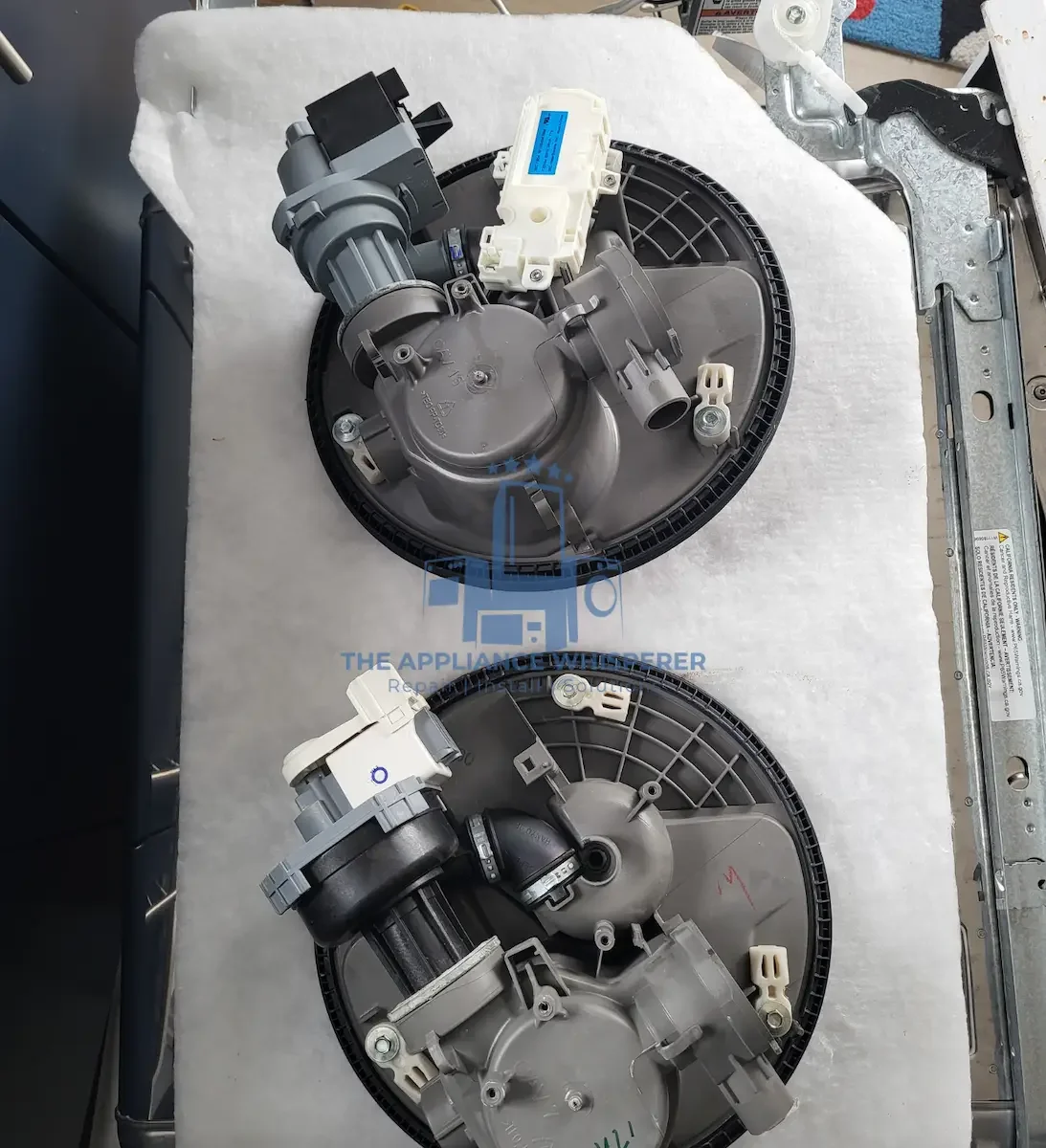 Two washing machine circulation pumps with motors and attached components placed on a white surface.