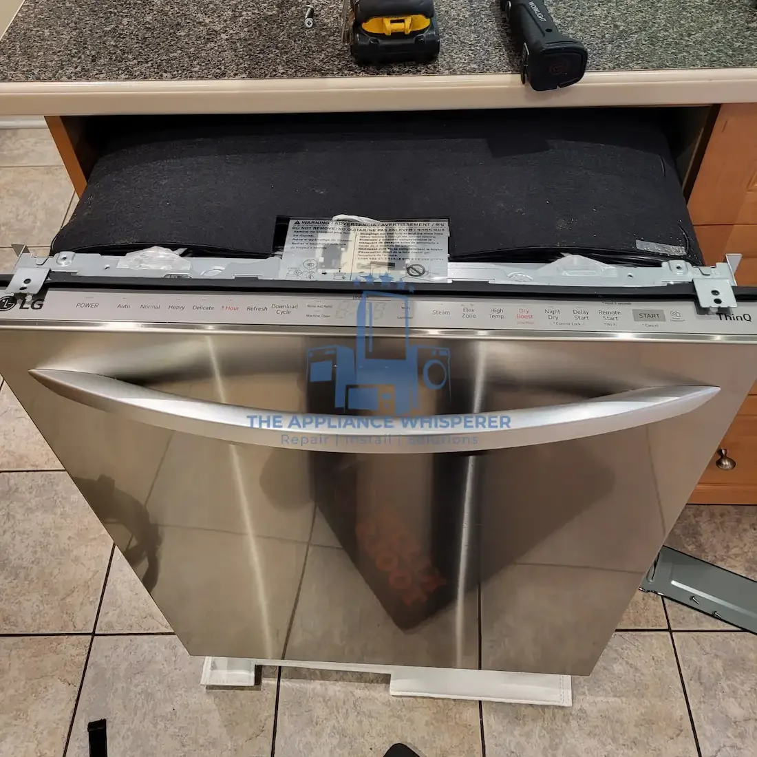 A stainless steel LG dishwasher with its top panel removed, showing internal components and control panel, on a tile floor.