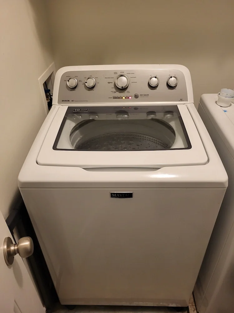 White top-loading Maytag washing machine in a laundry room next to a white dryer.