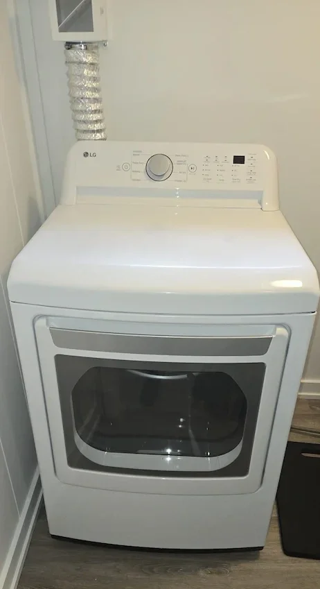 White LG washing machine with a digital control panel and a front glass door, located in a laundry room.