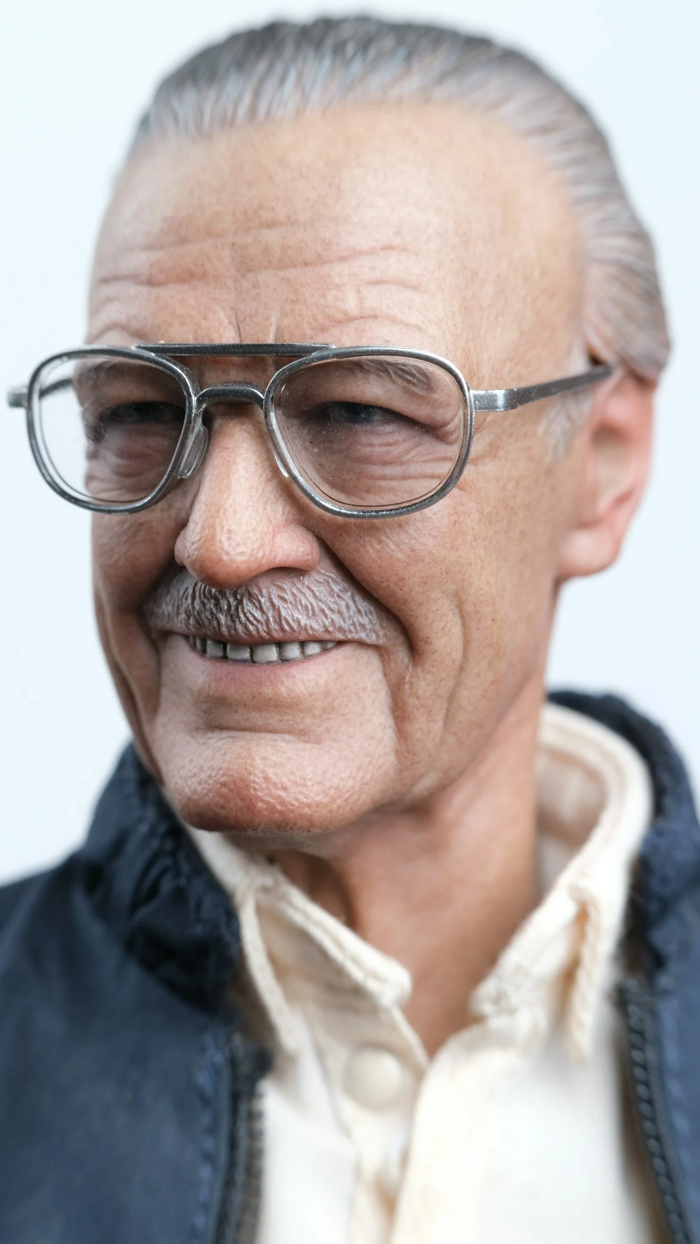 Close-up of a realistic statue of an elderly man with glasses, smiling.