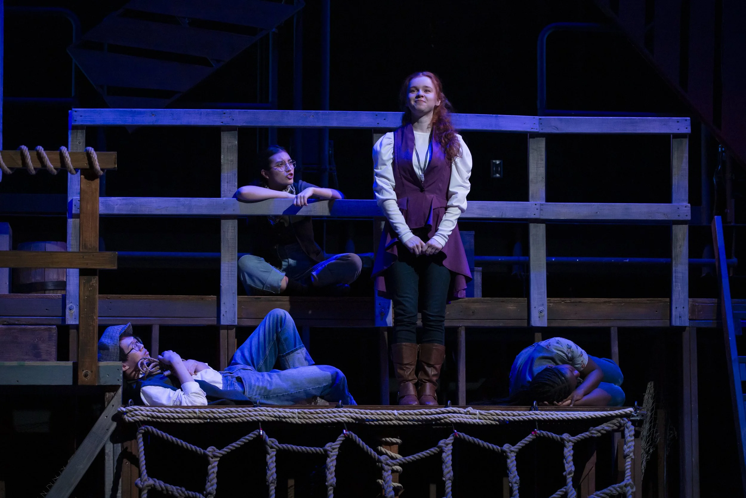 Young woman stands on the deck of a ship, surrounded by napping boys.