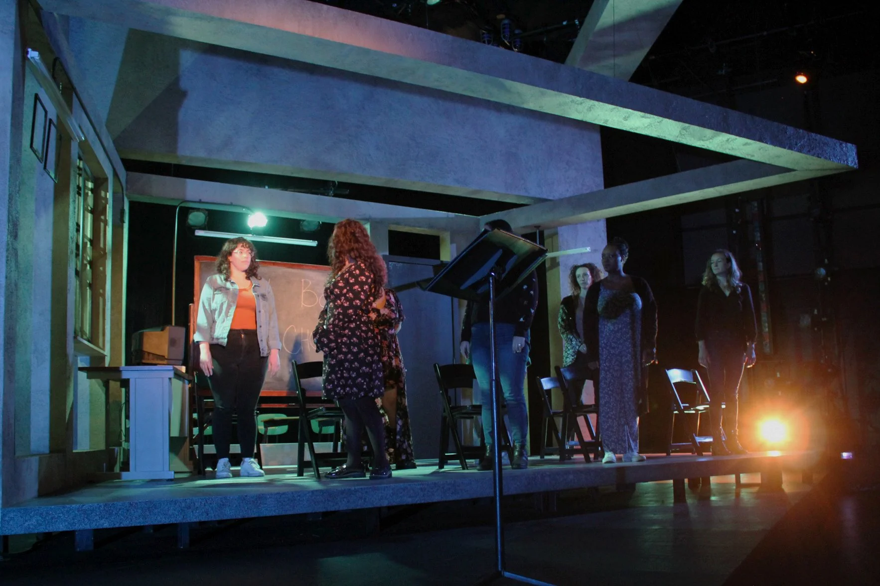 Seven women in shadow watch one illuminated woman.