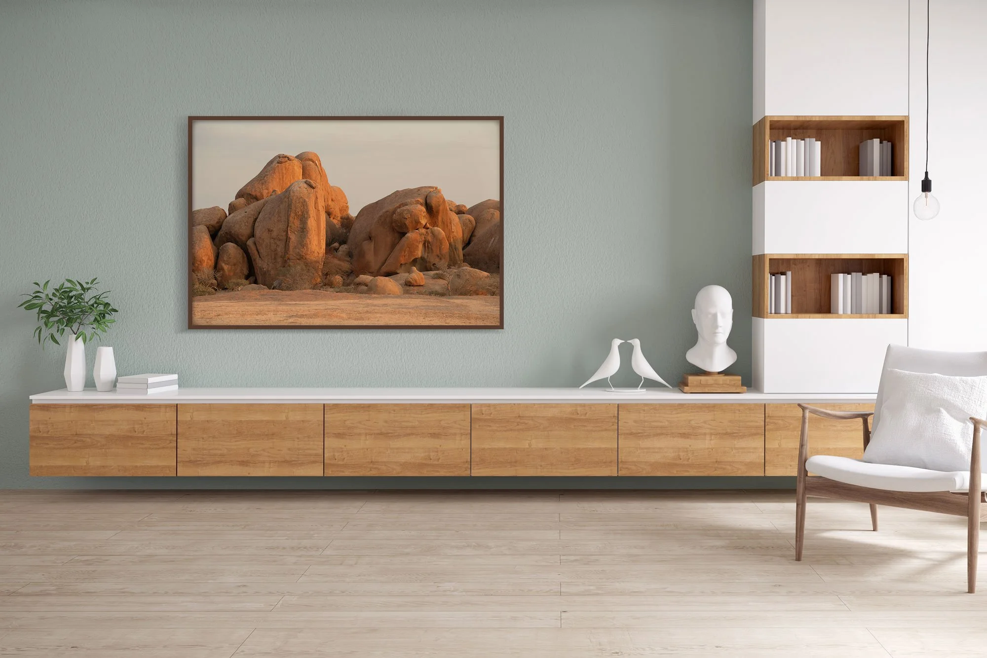 Moderner minimalistischer Wohnraum mit hellem Holzfußboden, weißen Wänden und einer geraden Holzkonsole. Über der Konsole hängt Bild von großen Felsen in der Wüste.