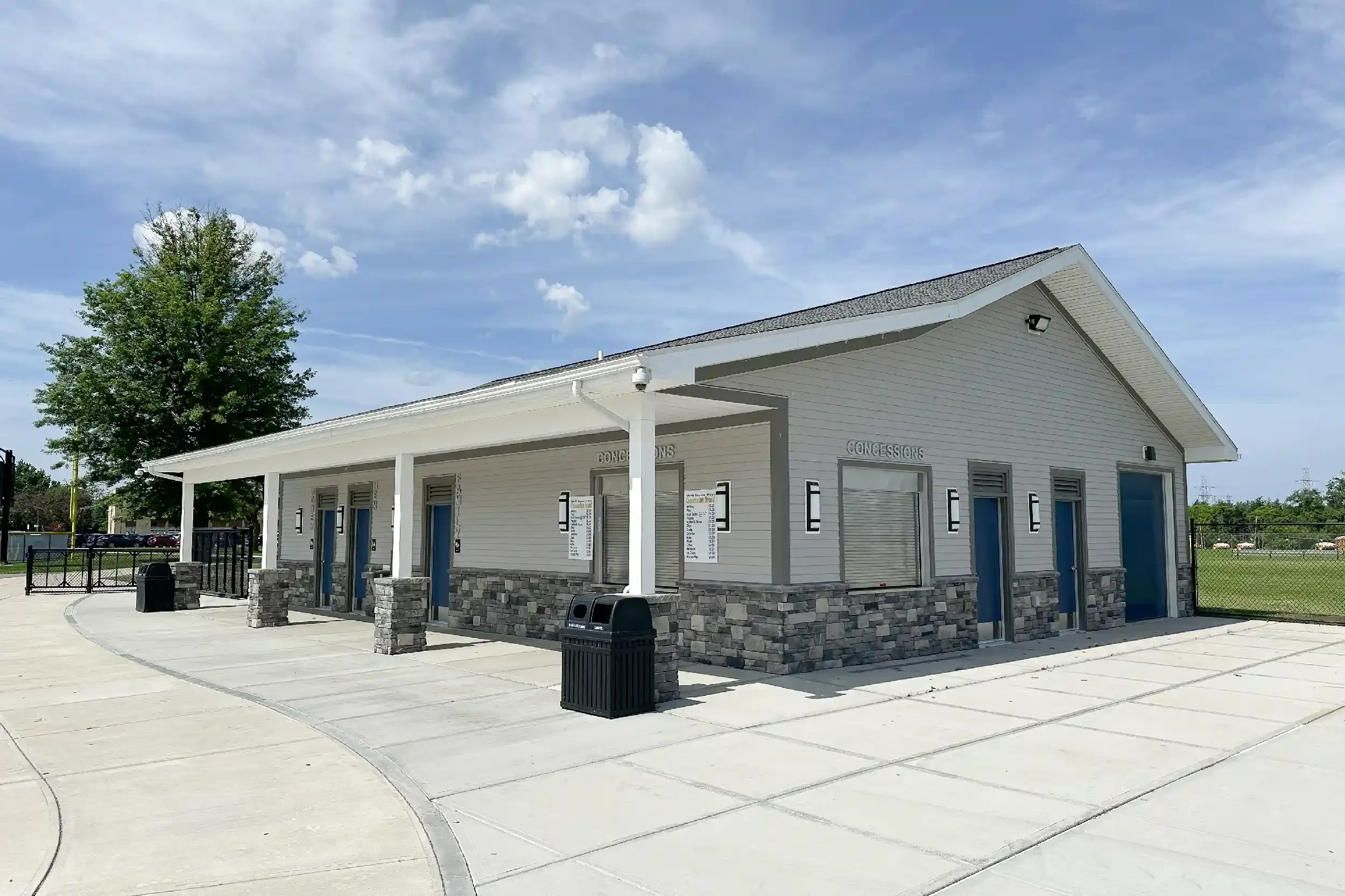 The exterior of a concession stand with grey siding, a deep porch along on side, and windows for ordering and pickup