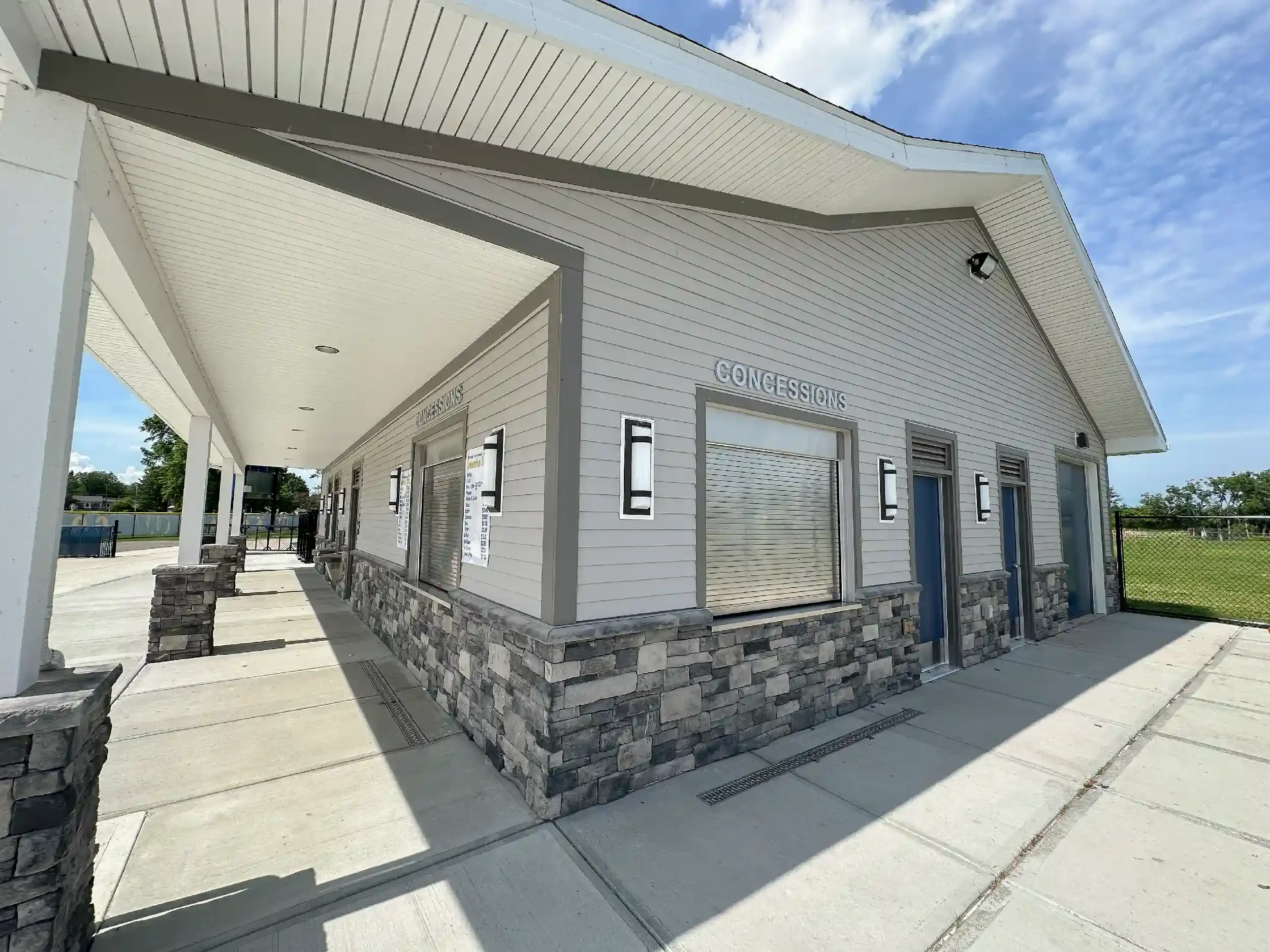 Closeup view of the exterior of a concession stand with grey siding, a deep porch along on side, and windows for ordering and pickup