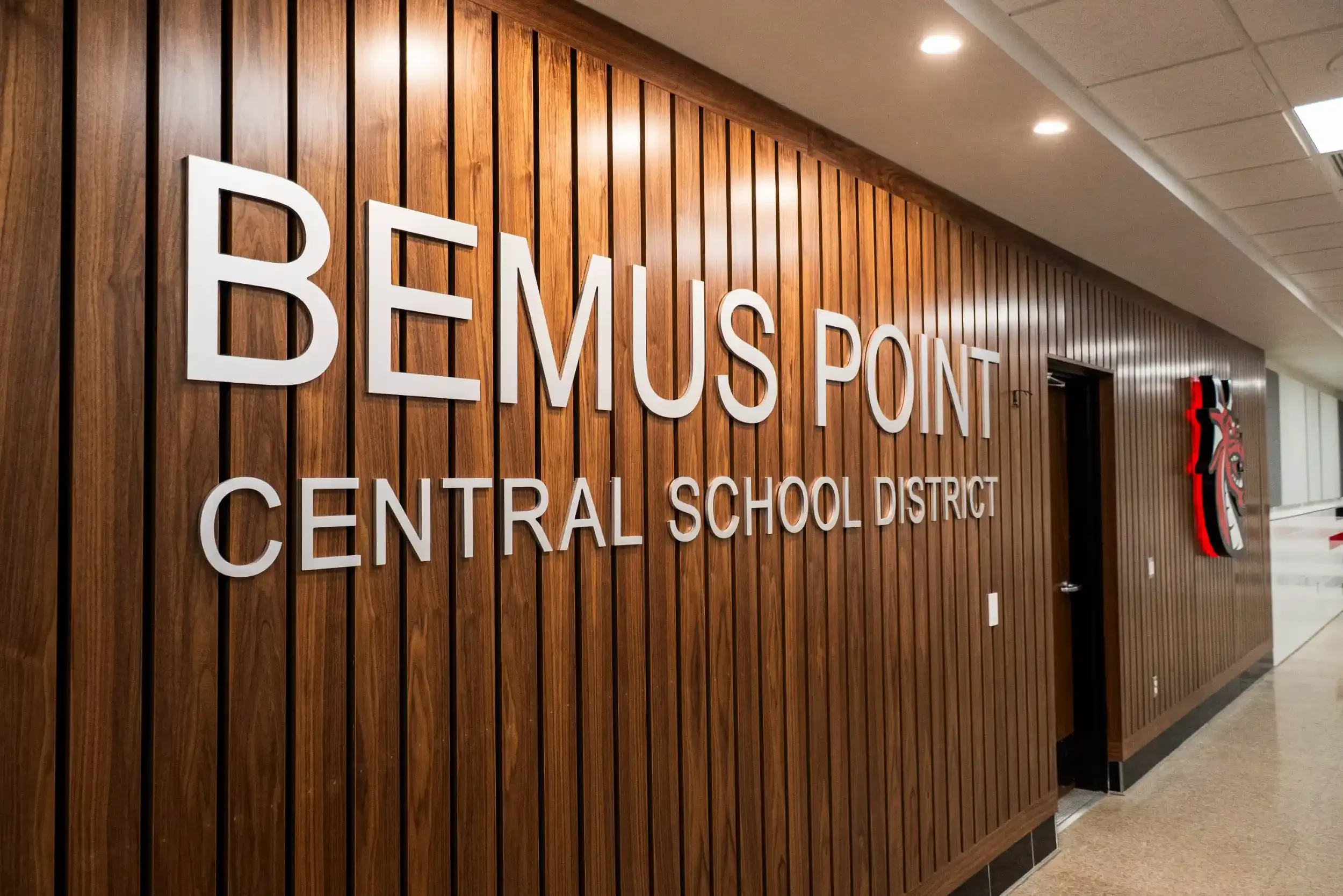 The school name and logo on a wood paneled wall at Bemus Point CSD.