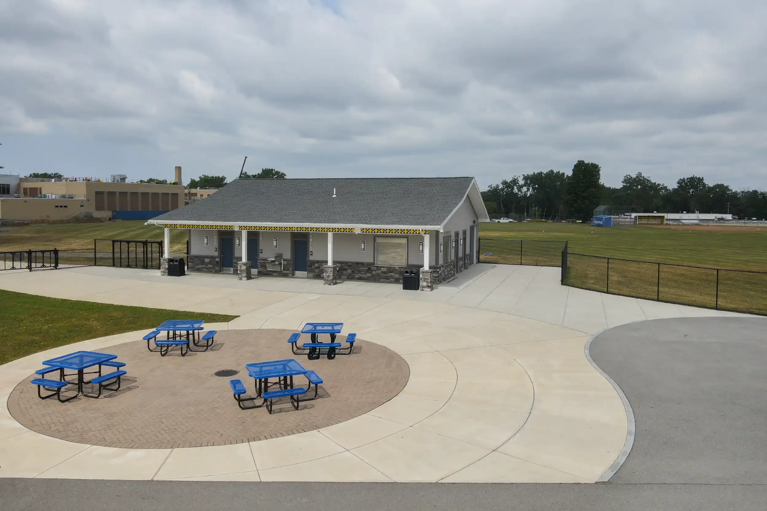 A concession stand with new concrete patio and four blue picnic tables