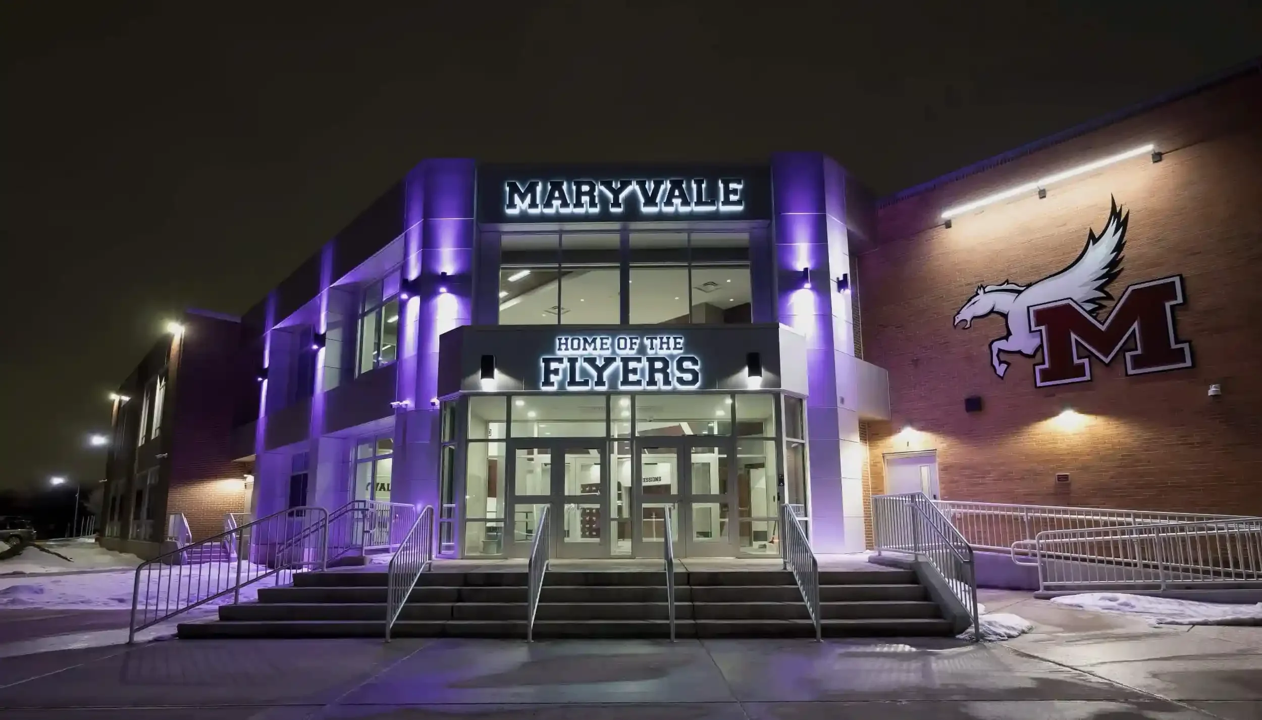 The exterior of the gymnasium entrance taken at night, showing purple uplighting
