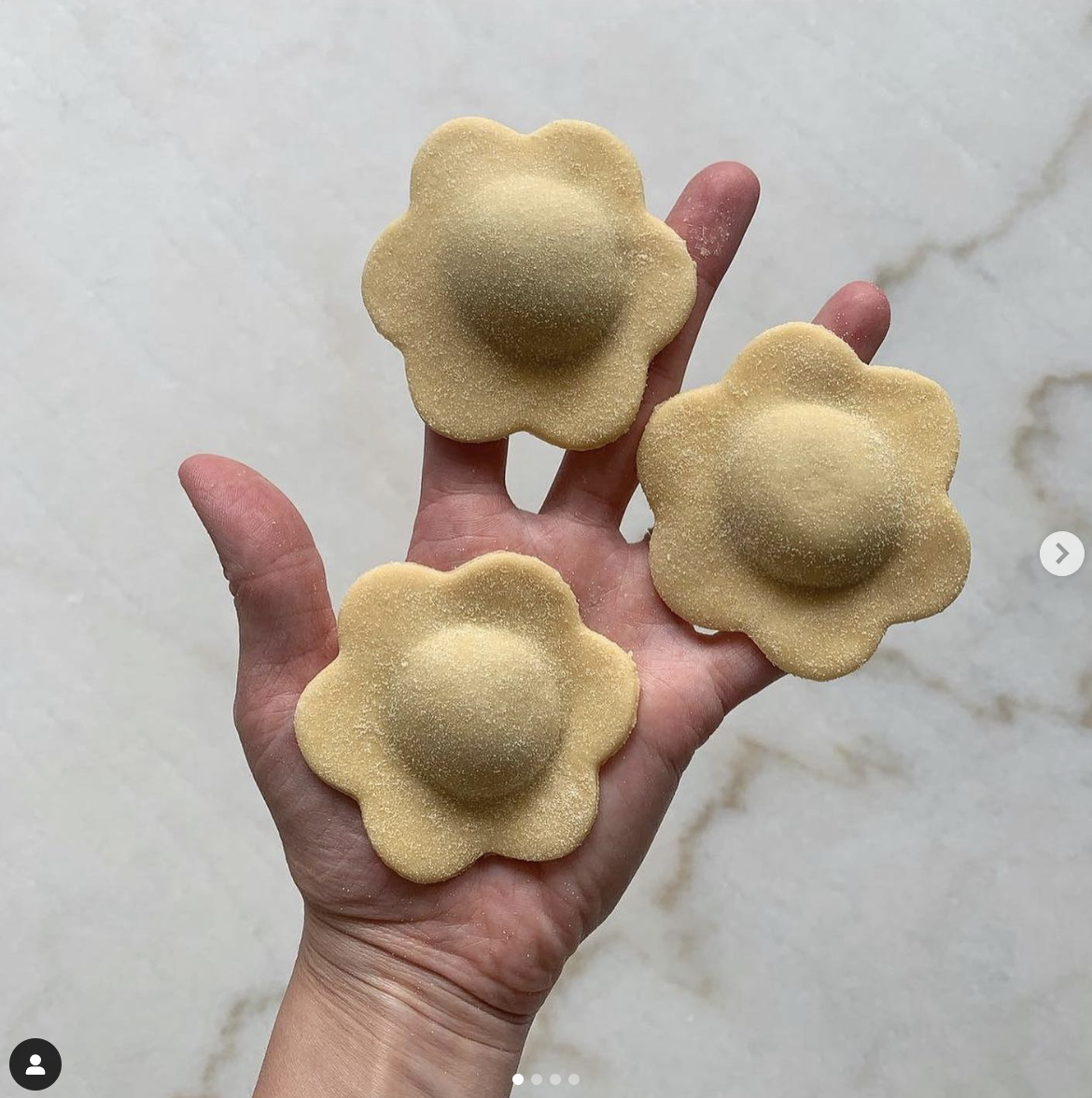 Tres flores de pasta con pétalos y un centro en forma de globo, colocadas en la mano de una persona.