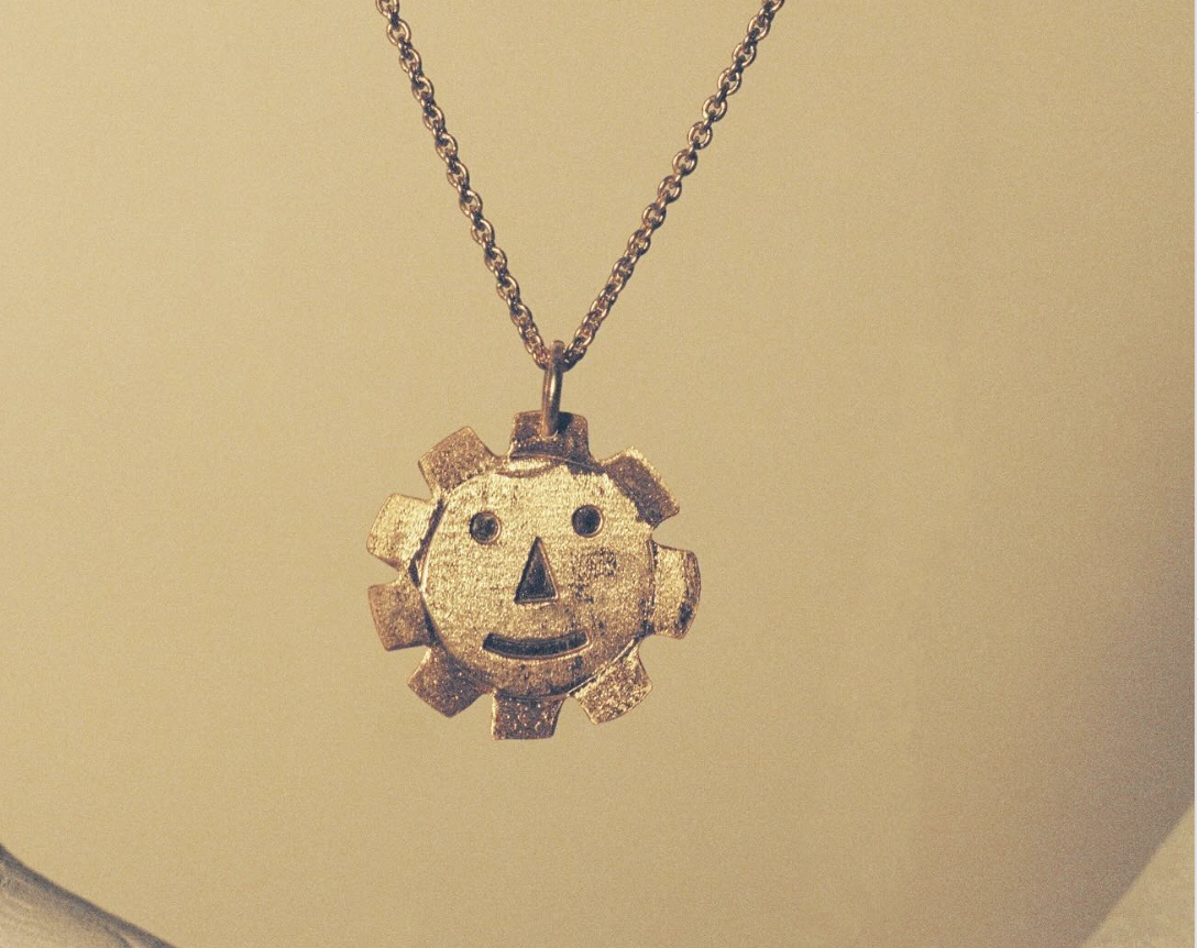 Colgante de cadena con un diseño de engranaje que tiene una cara con ojos, nariz y boca.
