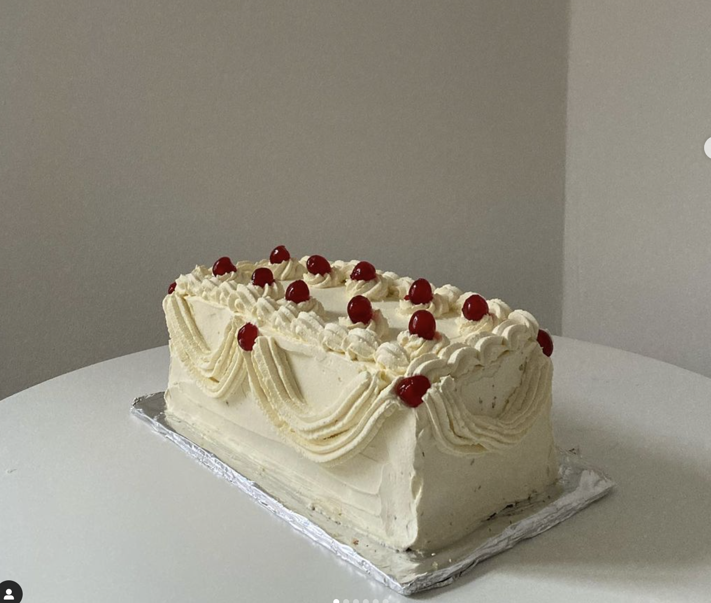 Pastel rectangular decorado con crema y cerezas rojas en la parte superior, colocado sobre una mesa blanca