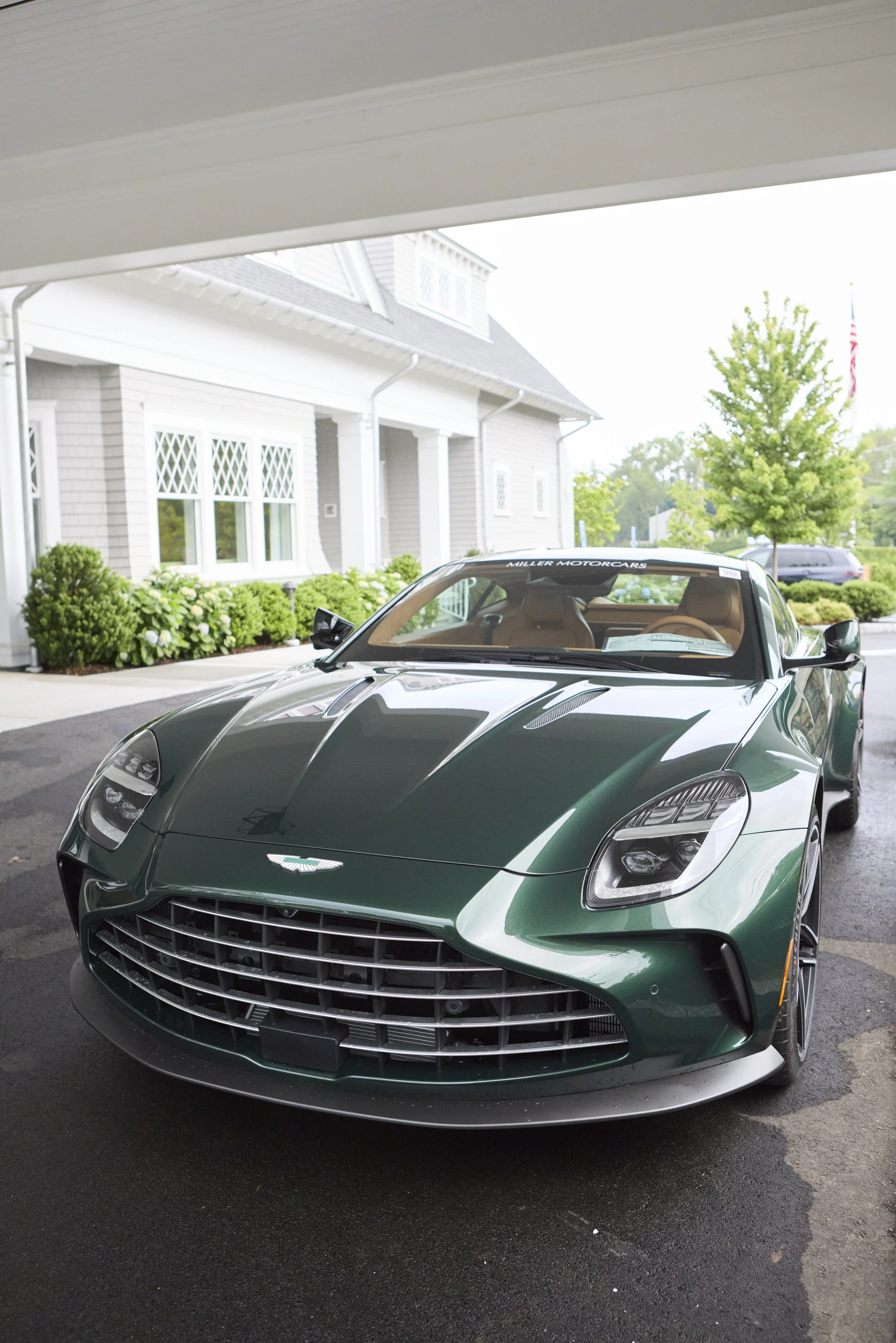 Green luxury sports car parked in a driveway with a house and trees in the background.