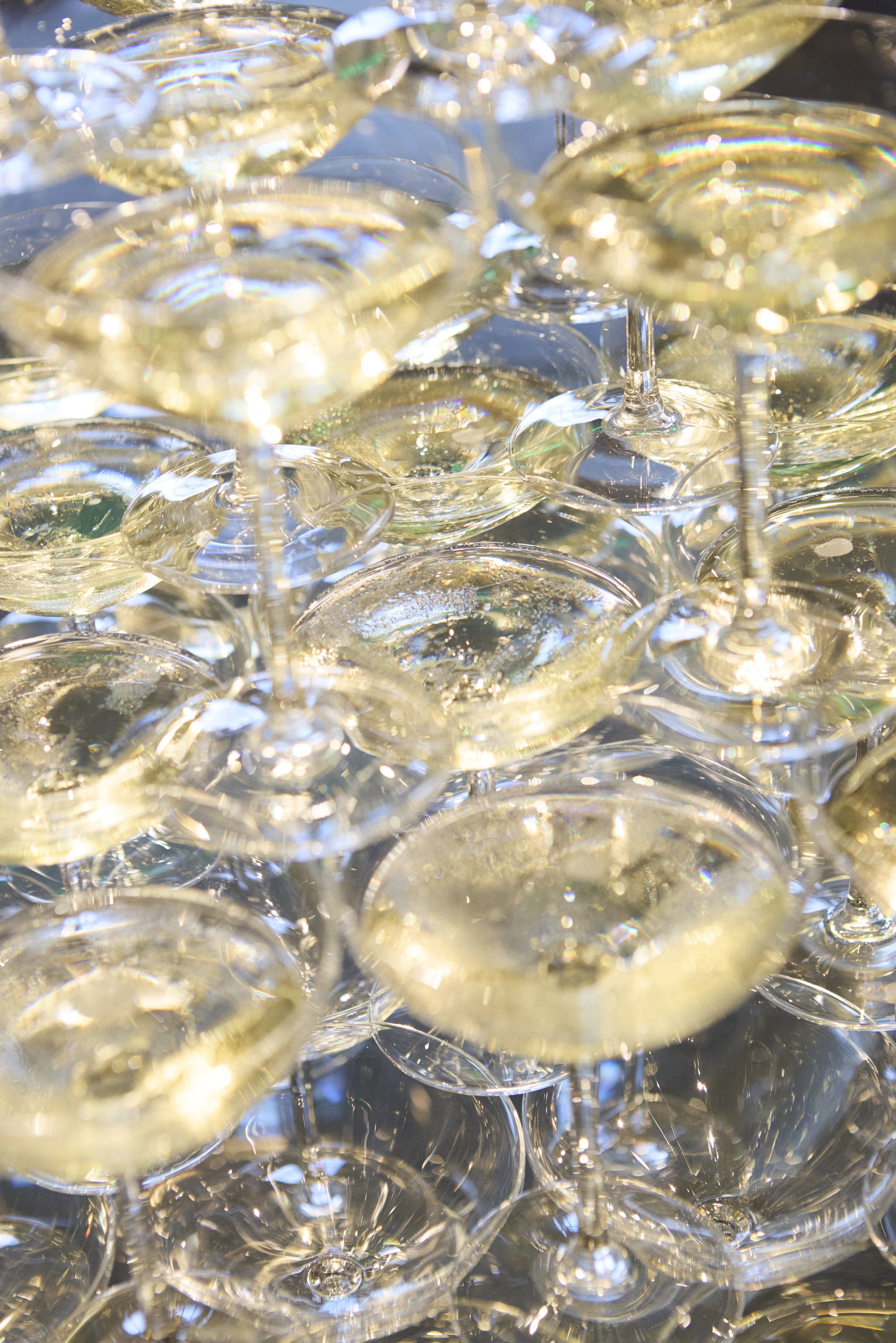 A large collection of champagne glasses filled with bubbly champagne, stacked closely together.