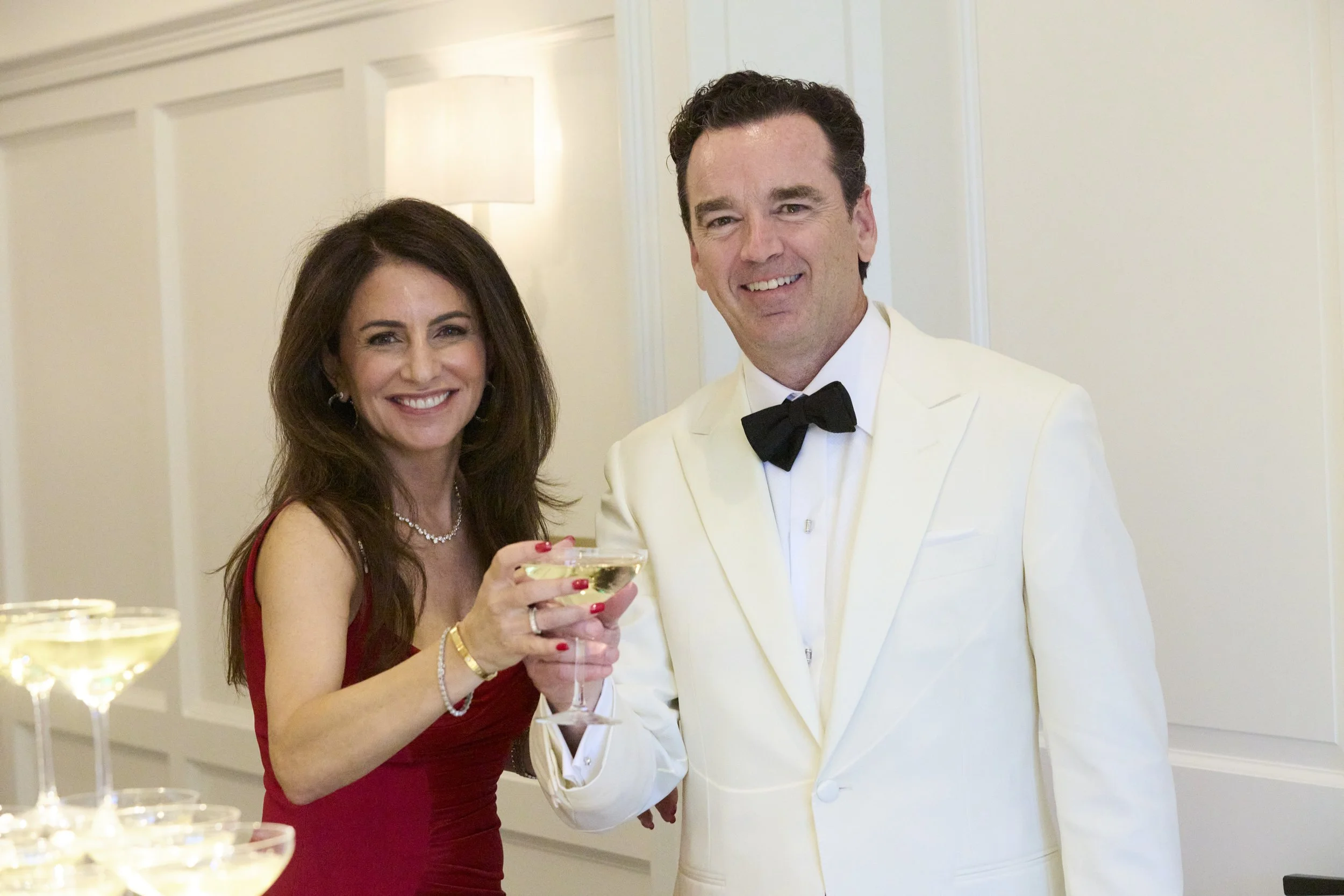 A woman and a man in formal attire celebrating at a party, holding a glass of champagne together.