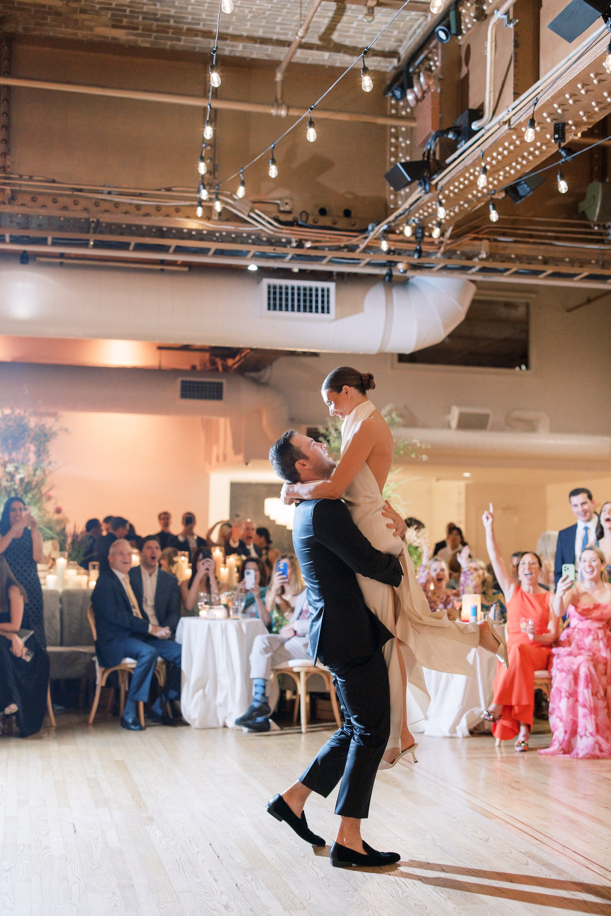 Bride and groom lifted during their first dance surrounded by guests at the Altman Building wedding reception in Chelsea NYC.