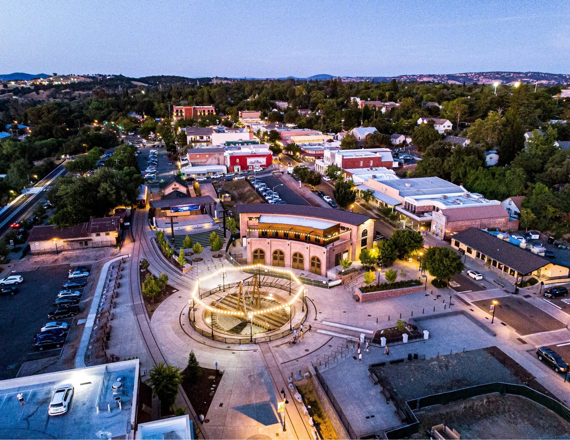 Aerial view of Historic Folsom in California at dusk with Sutter Street shops, the Folsom turntable plaza, and vibrant downtown lights.