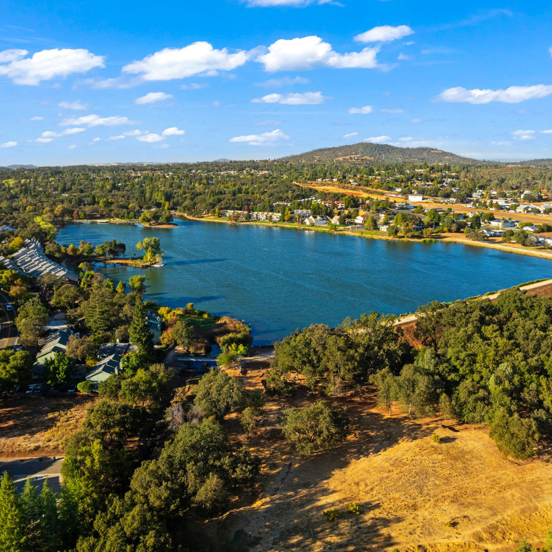 Aerial view of Cameron Park Lake in Cameron Park, California surrounded by homes, trees, and Sierra foothill landscapes.