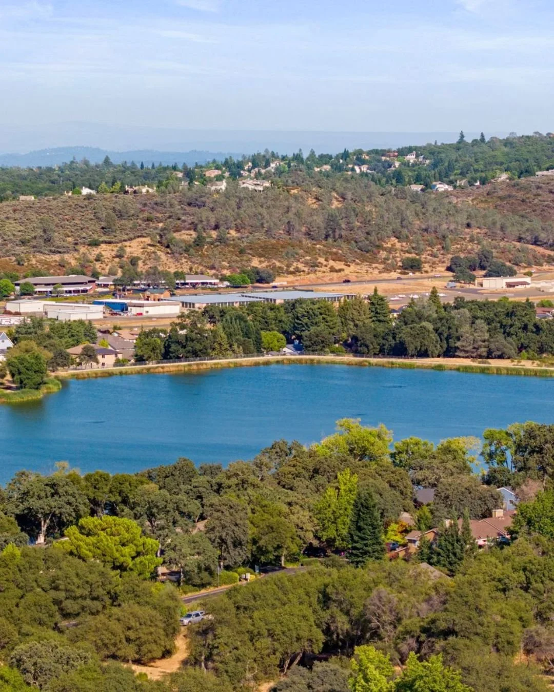 Aerial view of Cameron Park Lake in Cameron Park, California, surrounded by trees, homes, and foothill landscapes, a top local attraction and outdoor recreation spot.