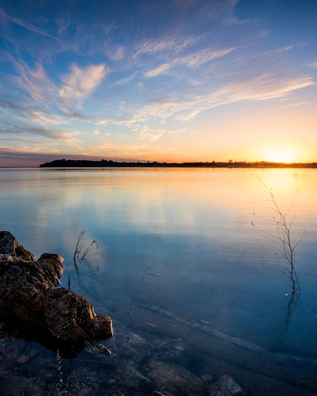 Sunset over Folsom Lake in California with calm water, rocky shoreline, and colorful sky reflecting on the lake.