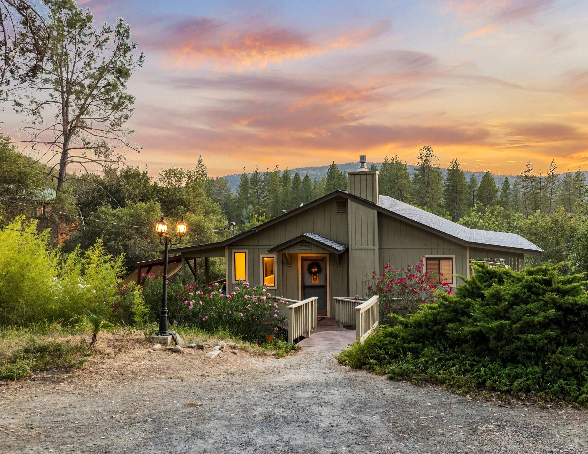 A cozy house with a front porch and a postage-stamp lawn, surrounded by greenery, at sunset with a colorful sky.