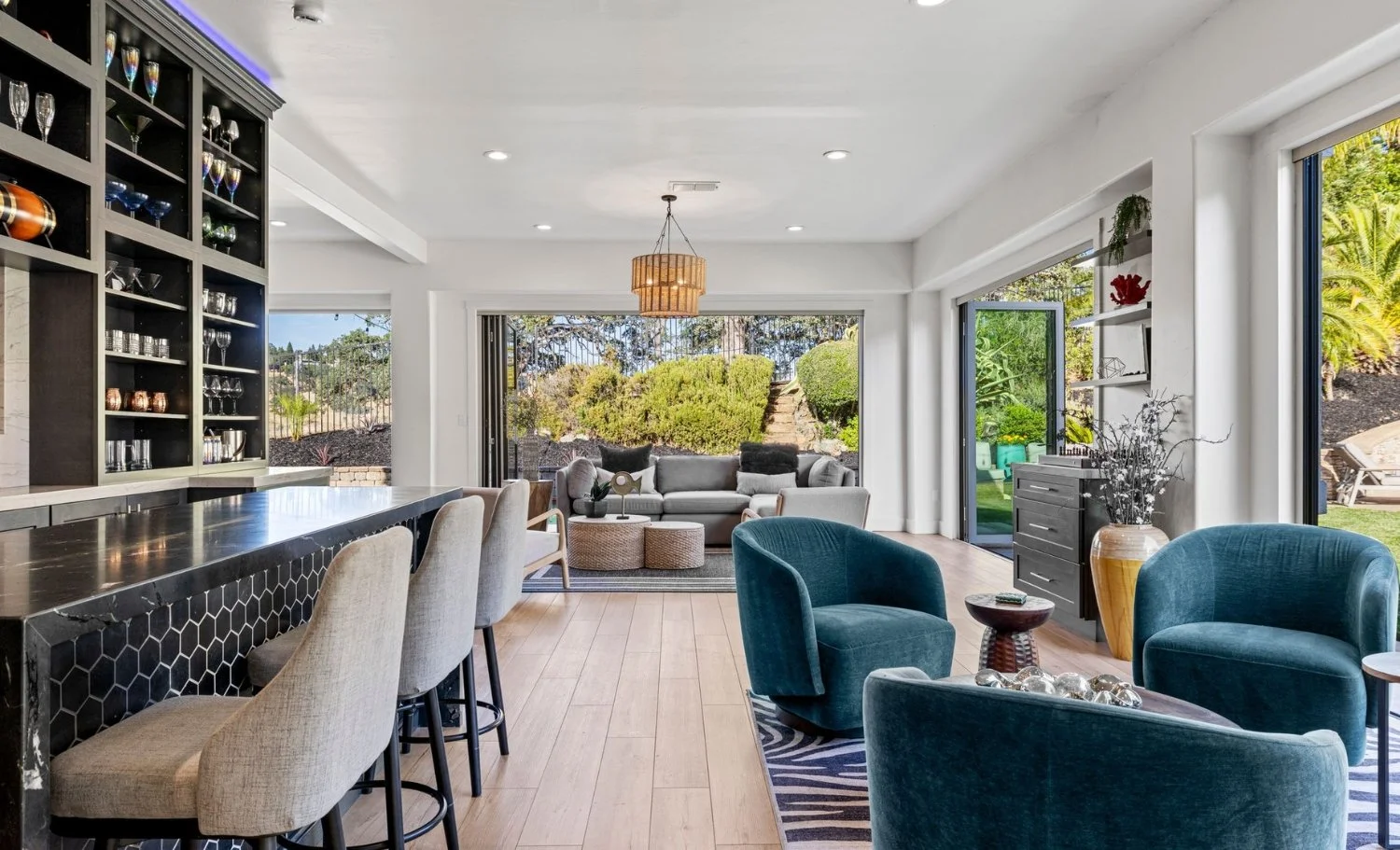 Modern open-concept living room with bar seating, stylish lounge chairs, and seamless indoor-outdoor flow to landscaped backyard in a luxury California home.